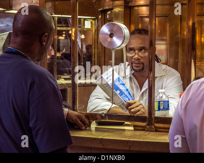 An African American railroad traveler seeks help from an African American at the information booth in Grand Central Station, NYC Stock Photo