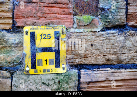 Yellow metal water hydrant sign covered in spiders webs and fixed too a stone wall. Stock Photo