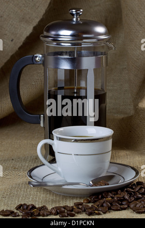 A cup of coffee on hessian with a cafetiere and beans