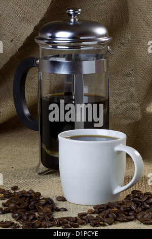 A mug of coffee on a hessian background with beans and a cafetiere