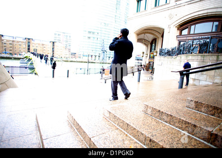 Man in black coat talking on mobile phone while walking down steps in Canary Wharf business district, Stock Photo