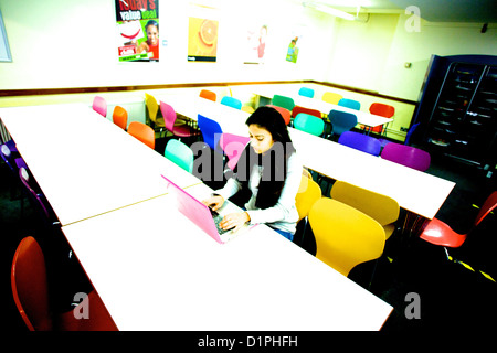 Girl using pink laptop computer in canteen with colorful chairs at SOAS, UCL, London Stock Photo