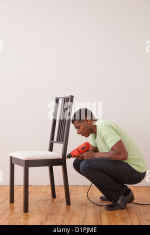 Black man using drill on chair Stock Photo