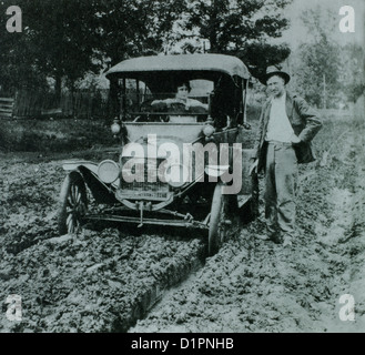 Woman in Ford Model T Car on Muddy Road With Man Standing Next to it, early 1900's Stock Photo