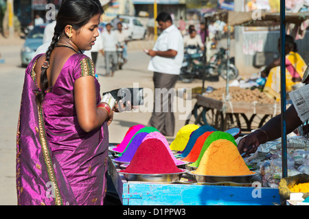 Indian woman buying coloured powder used for making rangoli designs at festivals from a cart on the street. Puttaparthi, Andhra Pradesh,  India Stock Photo