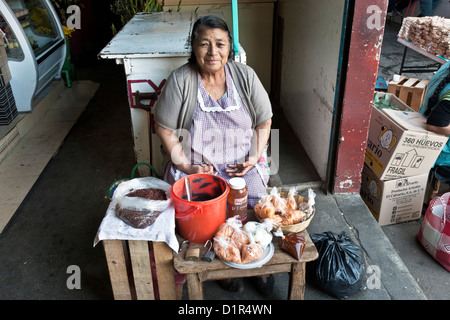 middle aged woman vendor selling fried grasshoppers frijoles & other prepared food at entrance to mercadoLa Merced market Oaxaca Stock Photo