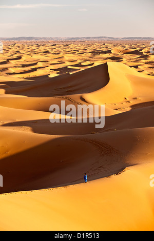 Morocco, M'Hamid, Erg Chigaga sand dunes. Sahara desert. Local Berber man on sand dune, background tourist camp, bivouac. Stock Photo