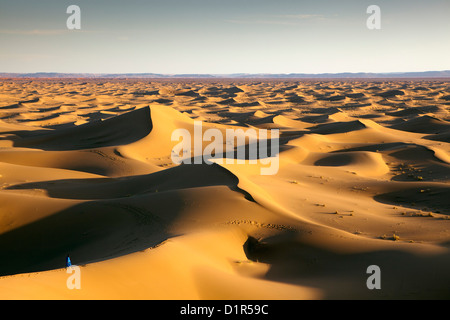 Morocco, M'Hamid, Erg Chigaga sand dunes. Sahara desert. Local Berber man on sand dune, background tourist camp, bivouac. Stock Photo