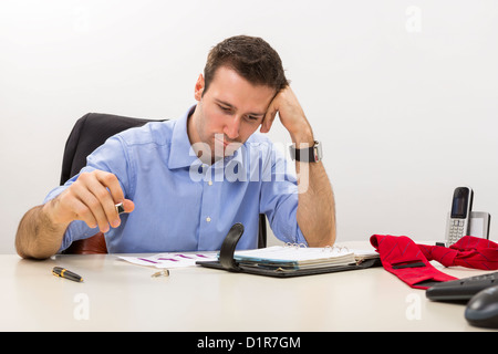 Young stressed manager analyzing some charts with hand at his temple. Stock Photo