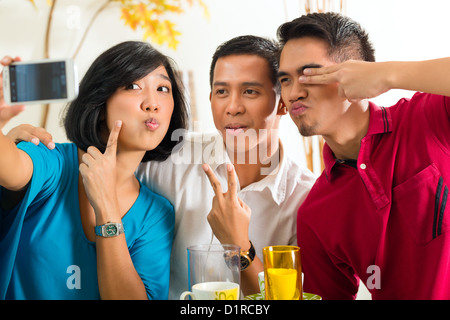 Asian friends, two men and a woman, having fun taking pictures with mobile phone Stock Photo