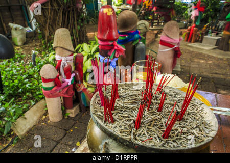 Jan. 4, 2013 - Bangkok, Thailand - Penises behind incense at the Lingam Shrine in Bangkok. The Lingam Shrine is a phallus garden behind the Swissotel Nai Lert Park Hotel, an exclusive 5 star hotel in Bangkok. Clusters of carved stone and wooden shafts surround a spirit house and shrine built by a Bangkok millionaire to honour Jao Mae Thap Thim, a female deity thought to reside in a banyan tree on the site. According to Bangkok legend, a woman who made an offering at the shrine had a baby after praying at the shrine, and it has received a steady stream of worshippers ever since.  Stock Photo