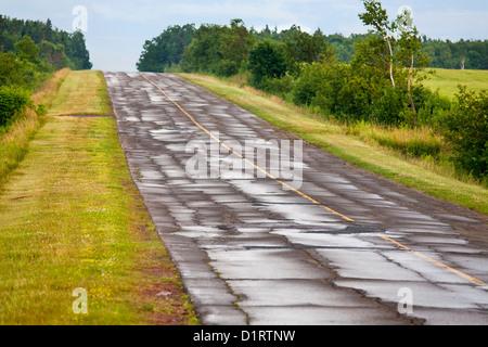 A paved asphalt road broken up from freezing and thawing. Cold patch is in the pot holes and wide cracks. Stock Photo