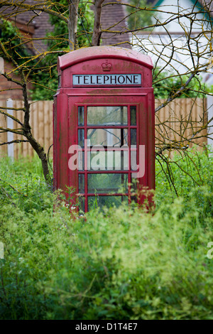 An old Red Telephone Box stands forlorn near a roadside in Worcestershire as it steadily loses it's battle with the environment Stock Photo