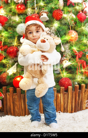 Picture of happy small boy holding teddy bear in hands on beautiful decorated Christmas tree background Stock Photo