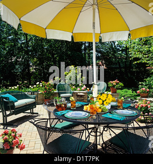 PATIOS Close up umbrella table and surrounding wicker furniture small stone wall defines patio area Yellow and white umbrella. Stock Photo