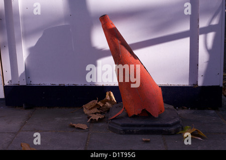 orange bollard bent & damaged in shadows, with hoarding behind , Stock Photo