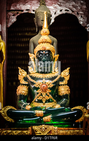 Medicine Buddha Wat Mai Suwannaphumaham Ornate Green Gold Luang Prabang Laos / LUANG PRABANG, Laos — A green Buddha adorned in elaborate gold filigree sits on an altar inside Wat Mai Suwannaphumaham. The figure's emerald hue traditionally identifies it as the Medicine Buddha, or Bhaisajyaguru, invoked by practitioners for healing and the relief of suffering. Its ornate royal attire — featuring a tiered crown and jeweled chest piece — departs from simple monastic robes to depict the Buddha in his cosmic, transcendent form, a decorative convention common to high-status Lao temple interiors. Wat  Stock Photo