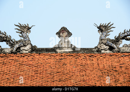 Temple Of Literature Traditional Dragon Sculpture Terracotta Tiles Hanoi Vietnam | HANOI, Vietnam — Two ceramic-inlaid dragons flank a sun disc on a terracotta roof ridge at the Temple of Literature, forming the "lưỡng long chầu nguyệt" (paired dragons facing the moon) motif seen throughout Vietnamese temple architecture. The design symbolizes cosmic harmony and royal authority. The complex was founded in 1070 and gained its Quốc Tử Giám academy, Vietnam's first national university, in 1076. Stock Photo