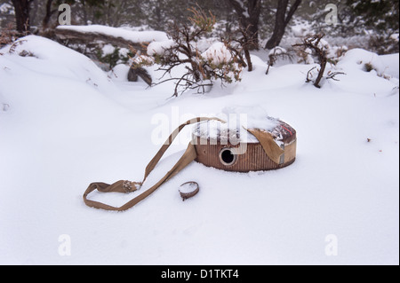 An empty vintage hiking and camping canteen lying in the snow in a remote part of the desert during a snowy winter. Stock Photo