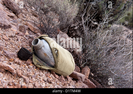 In a dry, remote wilderness area of the desert, an empty military canteen sits in front of dry brush Stock Photo