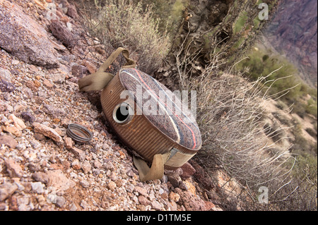 An old, empty canteen in a rugged desert wilderness provides an inference for dehydration and death. Stock Photo