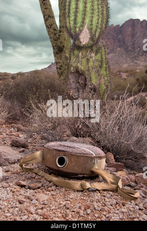 An old, vintage hiking canteen lies in a parched, dry desert, empty. Stock Photo