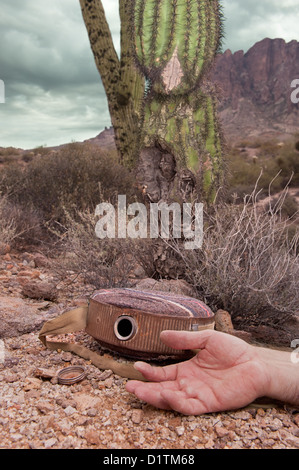 A hiker in the extreme wilderness succumbs to dehydration while in the remote desert, indicated by an old, empty canteen. Stock Photo