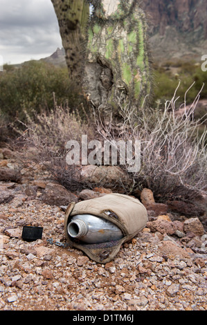 An old, vintage hiking canteen lies in a parched, dry desert, empty. Stock Photo