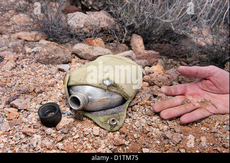 A hiker in the extreme wilderness succumbs to dehydration while in the remote desert, indicated by an old, empty canteen. Stock Photo