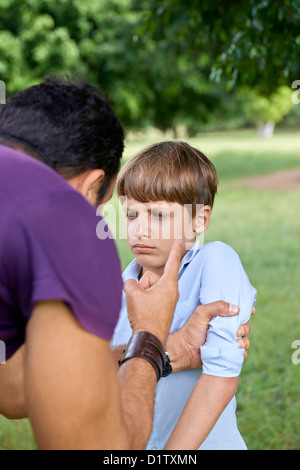 Young people and difficult parenthood, upset father scolding scared son while holding his arm. Waist up, focus on background Stock Photo