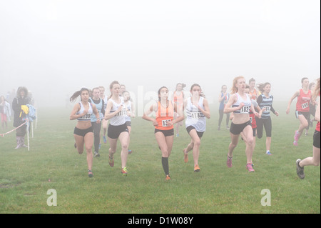 Kent Cross country running Championships under 15 girls youth running on trail path through wood in fog and misty conditions Stock Photo