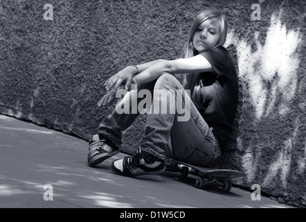 The girl with skateboard sitting against a wall. Shadow on a wall as a wing Stock Photo