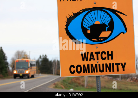 A school bus  passing a neighborhood watch sign beside a road Stock Photo