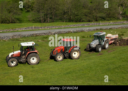 Tractors linked together pulling out a tractor and limespreader stuck in field. Cumbria, UK Stock Photo