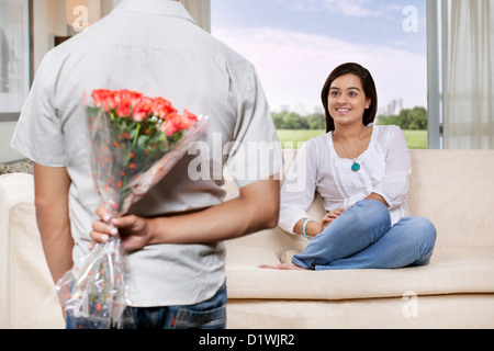 Man hiding bunch of flowers behind back while woman watching Stock Photo