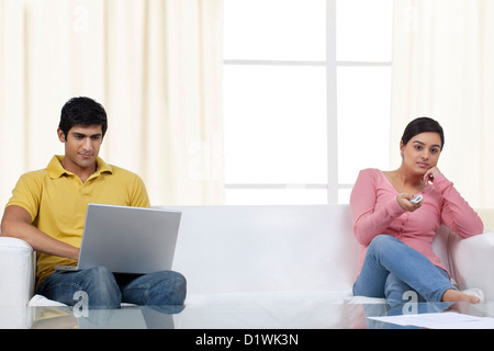 Man working on laptop while woman watching TV Stock Photo