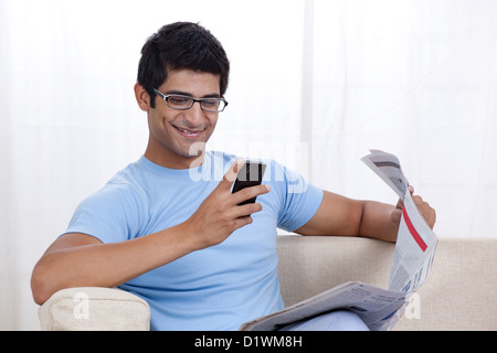 Happy young man looking at mobile phone while sitting on sofa Stock Photo