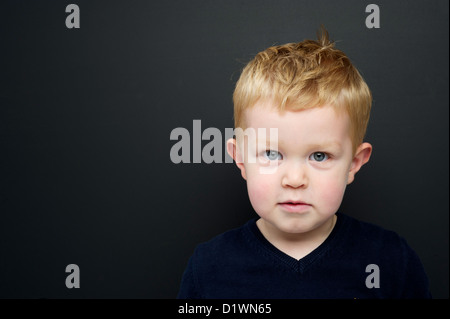 Smart young boy wearing a navy blue jumper stood in front of a blackboard