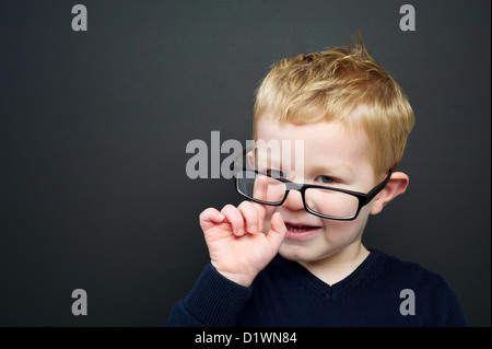 Smart young boy wearing a navy blue jumper and glasses stood infront of a blackboard