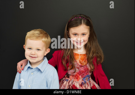 Smart young boy and girl stood in front of a blackboard smiling Stock Photo