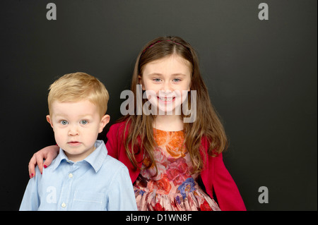 Smart young boy and girl stood in front of a blackboard Stock Photo