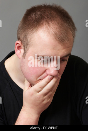 Young Man with hand over his mouth, deep in thought Stock Photo