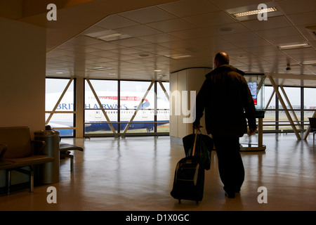 british airways 747 jumbo jet passing man with rolling travel case in terminal 1 passenger terminal building heathrow airport Stock Photo