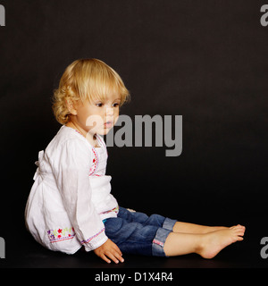 Two year old blonde infant girl in white shirt and denim on black background Stock Photo