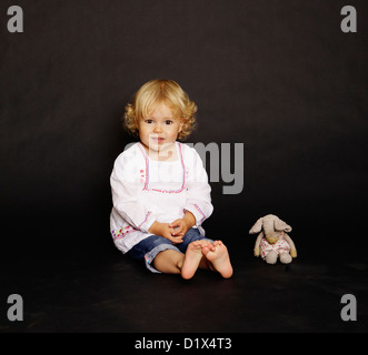 Two year old blonde infant girl in white shirt and denim on black background Stock Photo