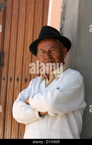 A well dressed Hispanic senior standing next to a building with arms crossed in Atuntaqui, Ecuador Stock Photo