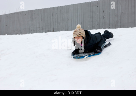 A woman slides down a small hill on a winter day. Stock Photo