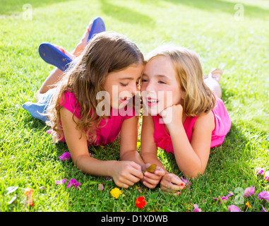 children friend girls playing whispering on flowers grass in vacations Stock Photo