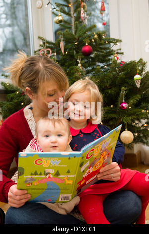 A young mother reading a welsh language book to her two small children at home, Wales UK Stock Photo