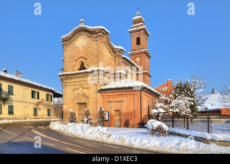 Old brick church near road through small town and snow on roadside in Piedmont, Northern Italy. Stock Photo